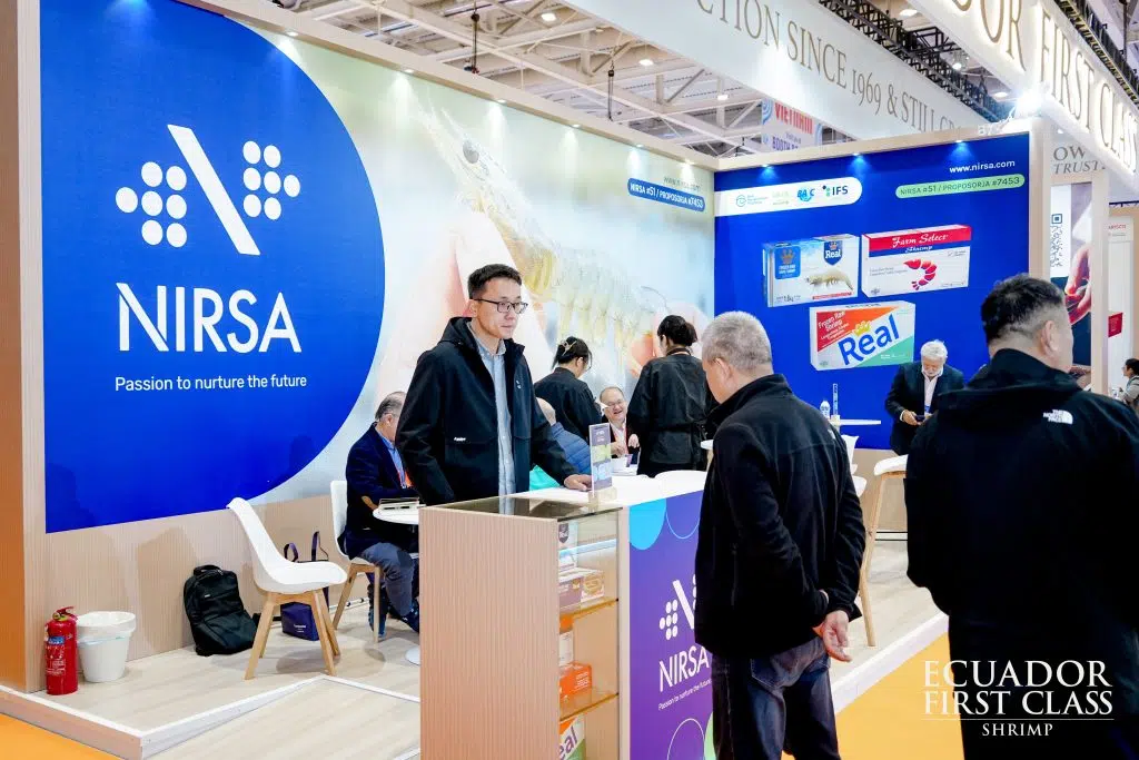 Stand de NIRSA en una feria: gran panel azul con el logo de la empresa, imagen de camarón y exhibición de productos Real, mientras visitantes conversan en el área de atención.